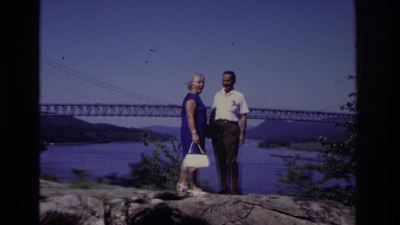 Couple standing on rocks with a suspension bridge and waterway behind them.