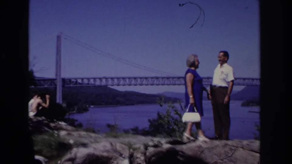 A 1968 home-movie frame shows the couple turned toward each other on the overlook, with a seated person partly visible at left.