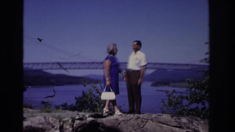 The couple stands close together at the overlook in the stated 1968 travel footage, framed by shrubs and a distant bridge view.