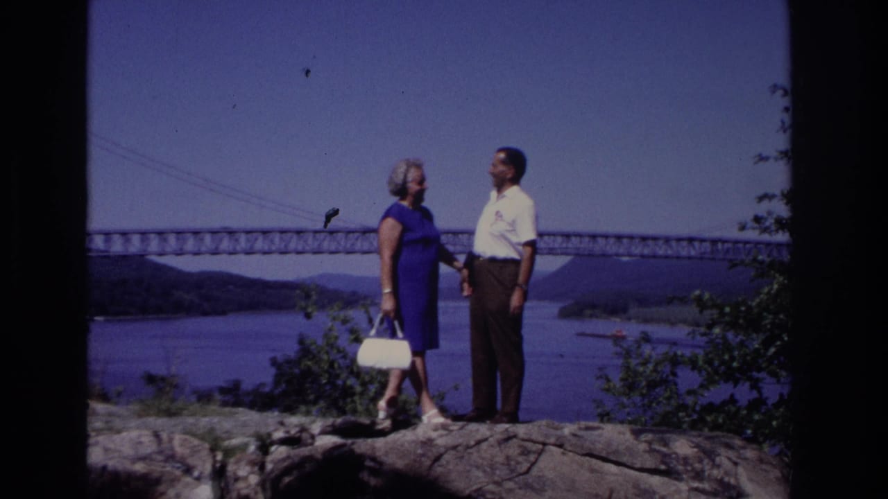 1968 8mm home-movie frame from Ocean City, New Jersey, showing two adults talking on a rocky overlook with a bridge and water behind them.