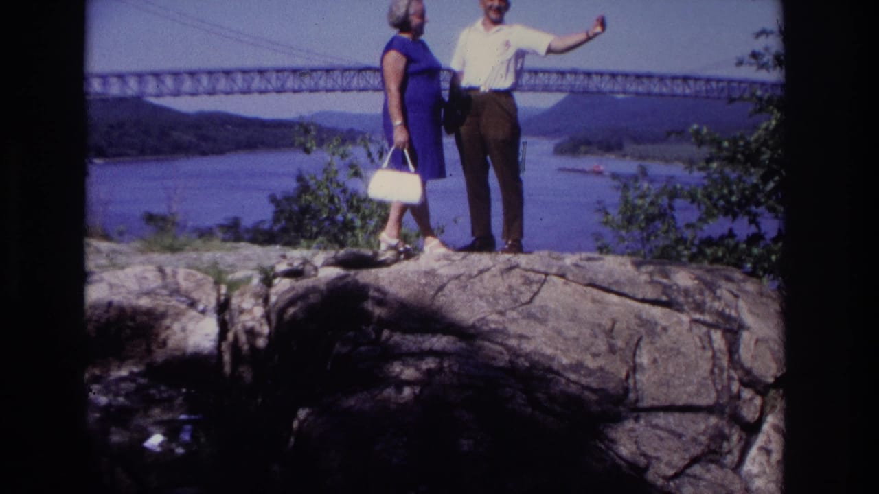1968 Ocean City, New Jersey home-movie frame showing a couple on rocks above water with a long bridge in the background.