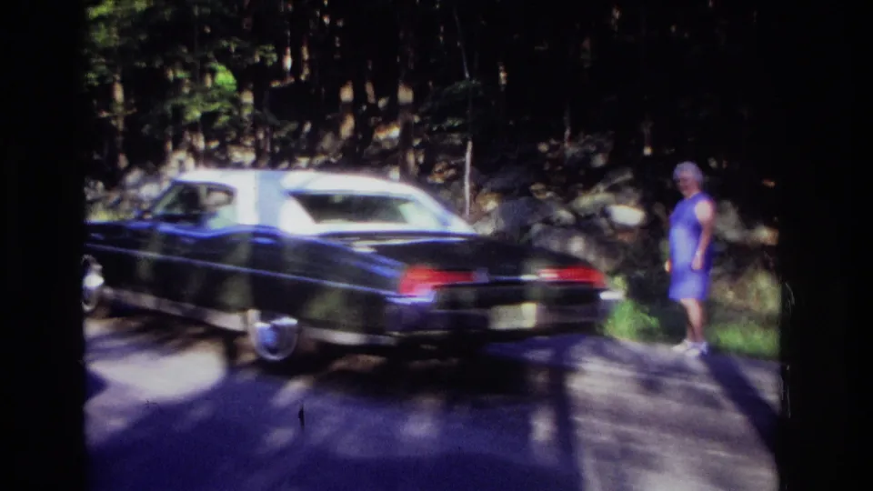 1968 Ocean City, New Jersey home-movie frame with a dark 1960s car passing a woman and deer on a forest road.