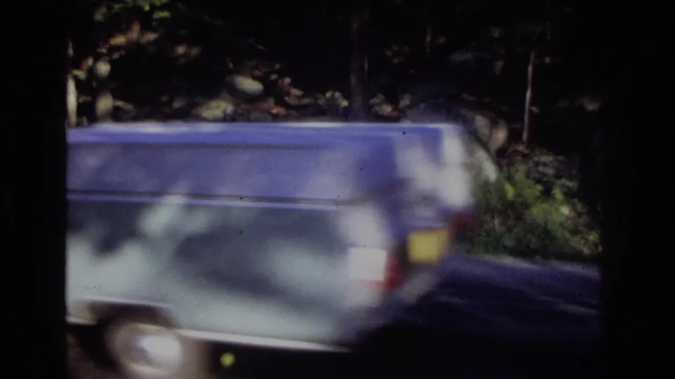 1968 Ocean City, New Jersey 8mm frame dominated by a blurred blue car passing along the wooded roadside.