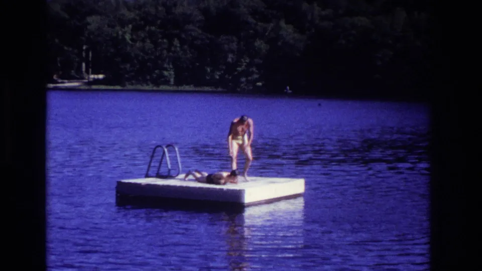 1968 Ocean City, New Jersey 8mm frame showing one person bending near another lying on a floating swim platform.
