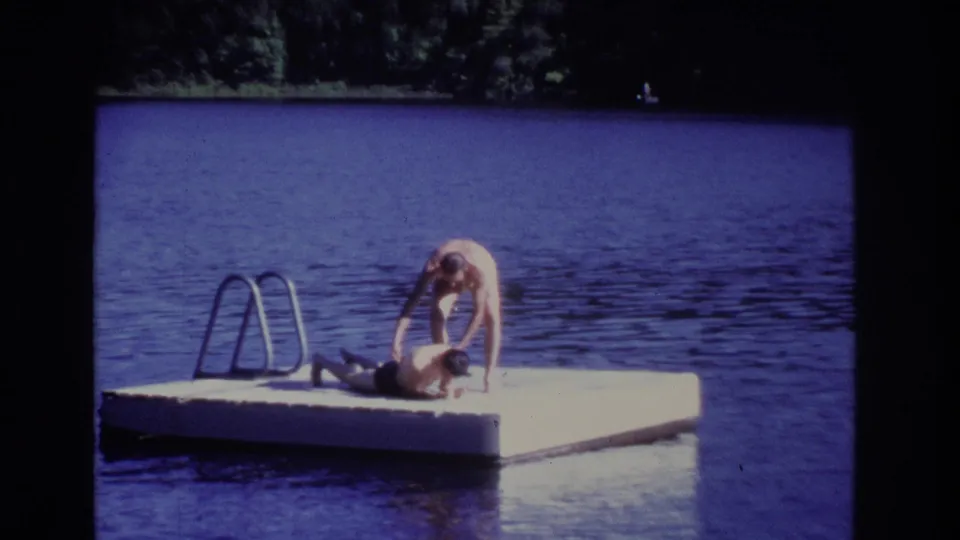 1968 Ocean City, New Jersey home-movie frame with two people on a floating lake dock beside a metal ladder.