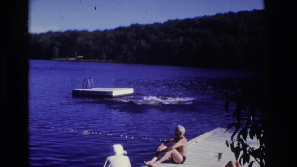 1968 Ocean City, New Jersey home-movie frame showing dockside swimmers, blue lake water, and a floating swim platform near a wooded shore.