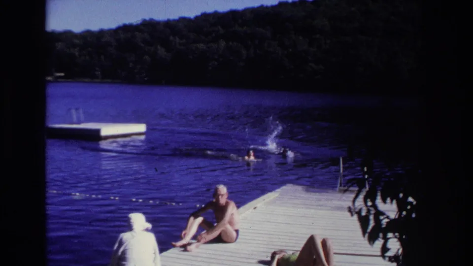 1968 Ocean City, New Jersey home-movie frame showing swimmers splashing beside a wooden dock with seated bathers in the foreground.