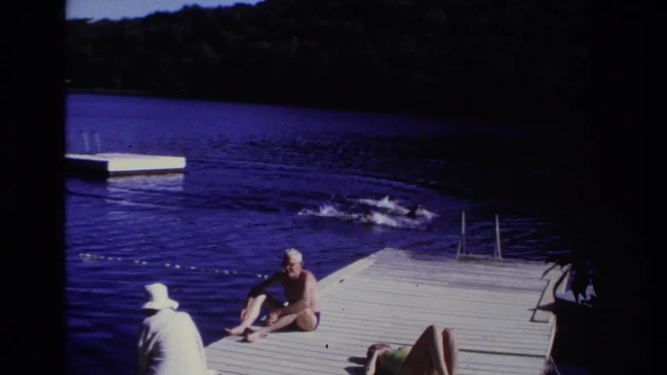 1968 Ocean City, New Jersey frame of swimmers near a dock, with seated adults, blue lake water, and a floating platform in the background.