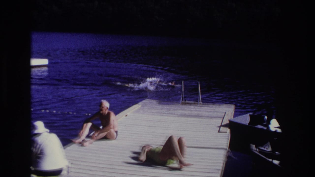 1968 Ocean City home-movie frame showing a seated man, sunbathing woman, and swimmers near a dock ladder.