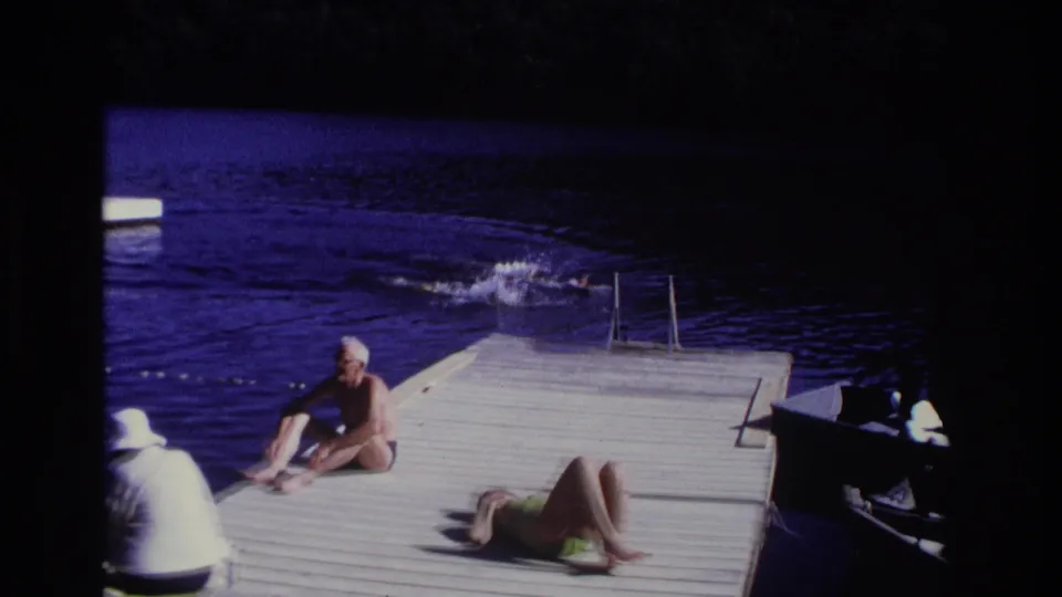 1968 Ocean City home-movie frame showing a seated man, sunbathing woman, and swimmers near a dock ladder.