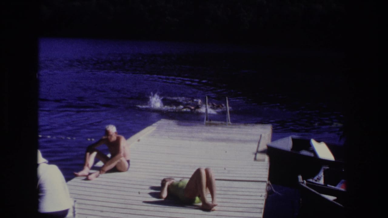 Swimmers splash in the water while adults sit and lie on a dock.