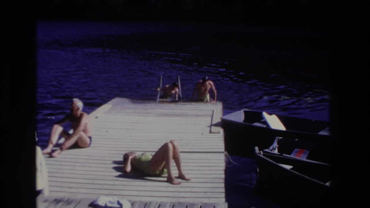 1968 Ocean City dock view with two swimmers at the ladder, a seated white-haired man, a sunbathing woman, dark water, and a moored small boat.