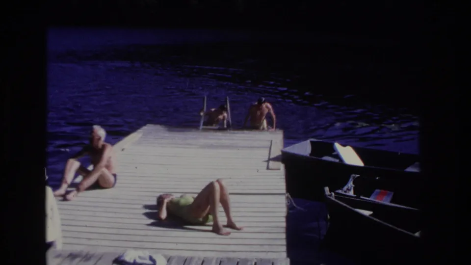 1968 Ocean City dock view with two swimmers at the ladder, a seated white-haired man, a sunbathing woman, dark water, and a moored small boat.
