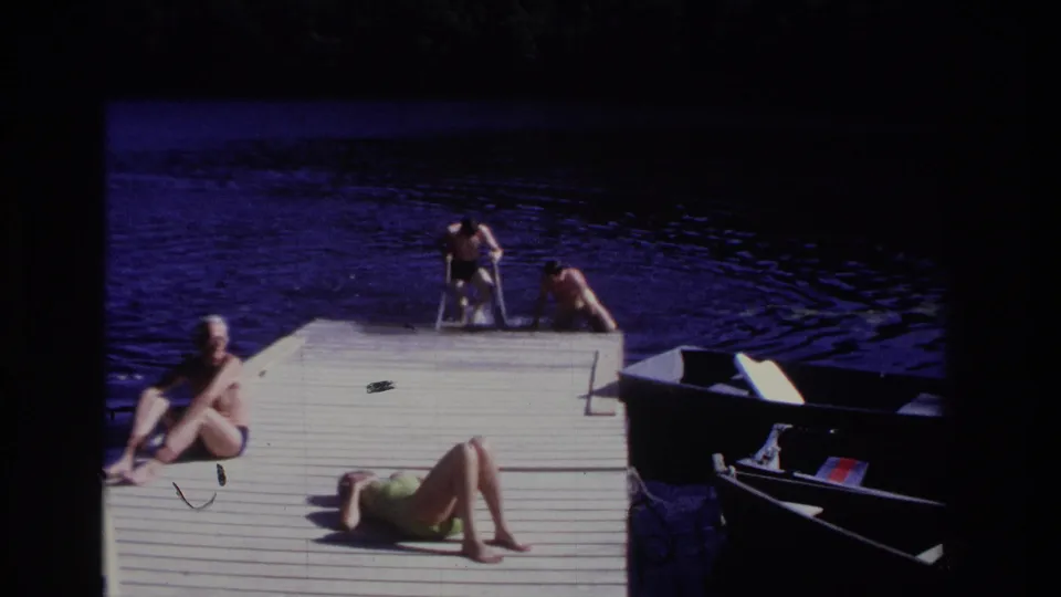 Final 1968 Ocean City frame showing two swimmers at the dock edge, a seated man, a woman in green sunbathing, dark water, and a small boat.