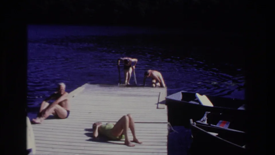 1968 Ocean City home-movie frame showing adults on a lakeside dock, including a seated man, a reclining woman, and two people near the water.
