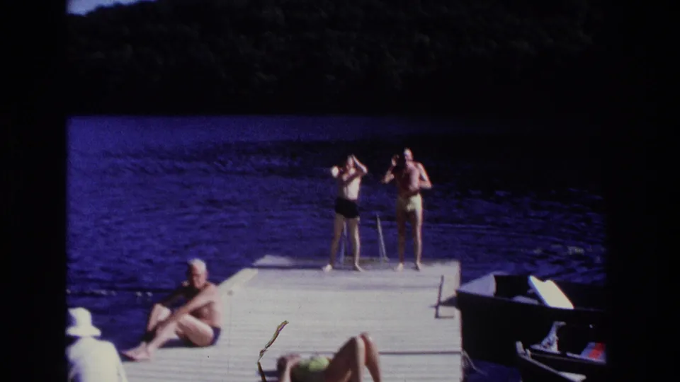 Home-movie frame from Ocean City in 1968 showing adults on a wooden dock, with two standing near the end and others relaxing closer to camera.
