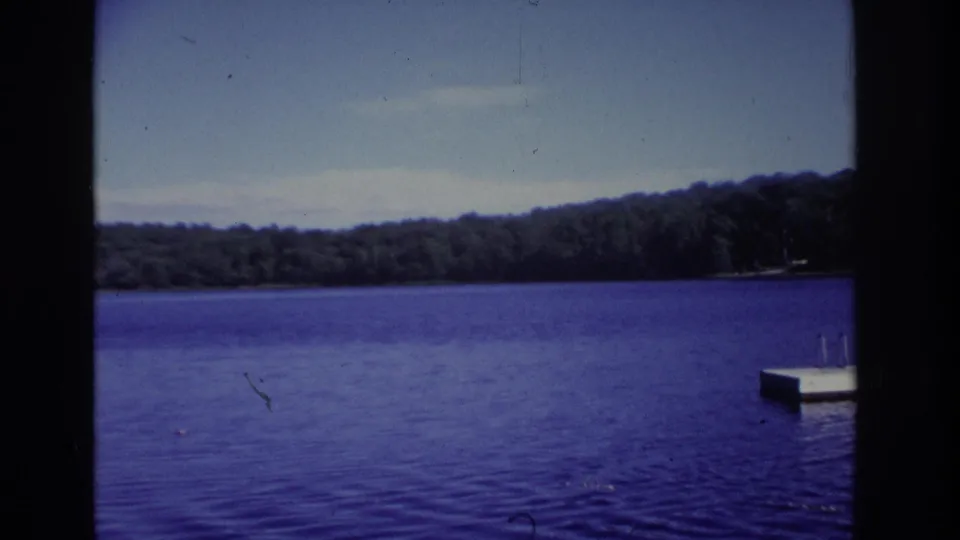 1968 Ocean City, New Jersey home-movie frame with calm blue water, distant trees, hazy sky, and a swim platform at frame right.