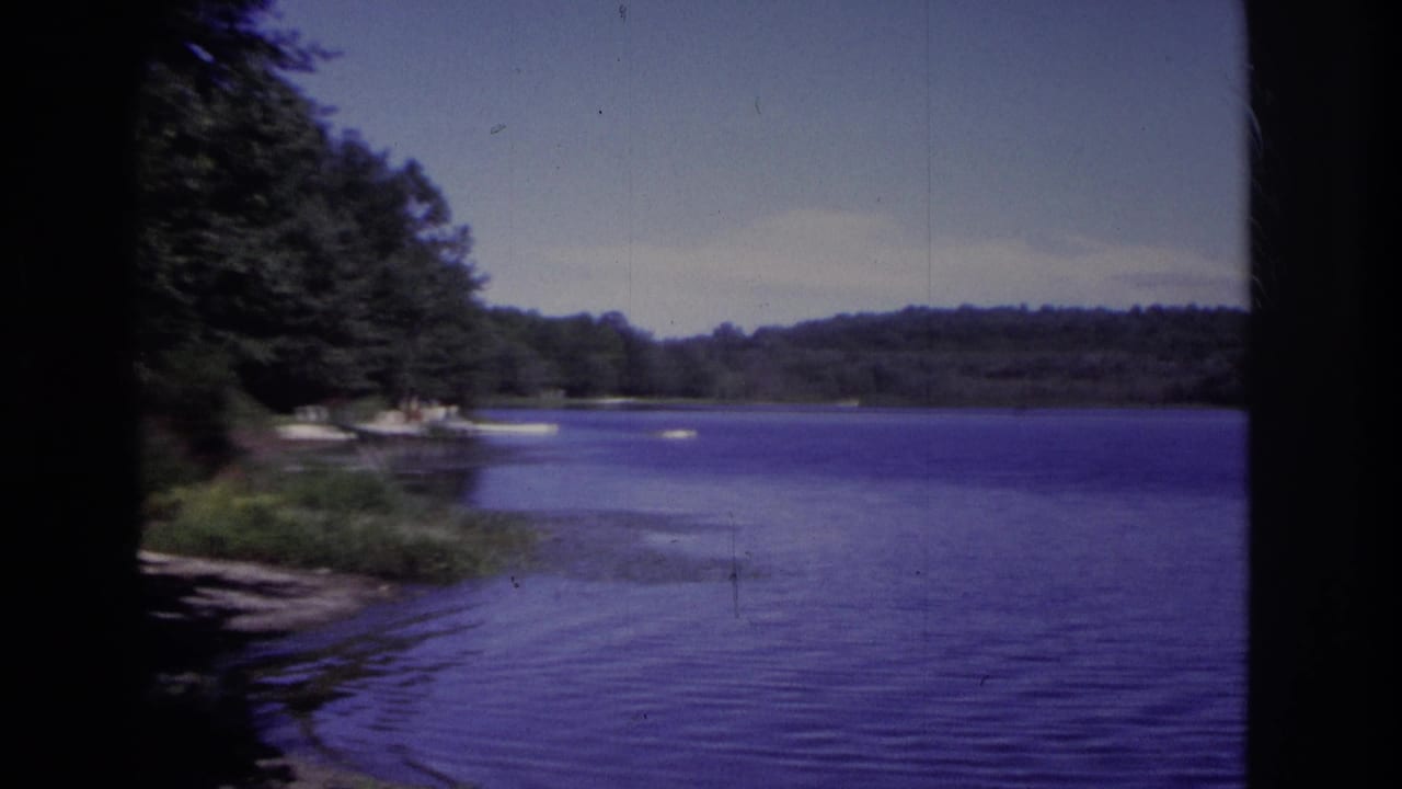 1968 Ocean City, New Jersey home-movie frame looking across rippled lake water toward trees, low hills, and small boats near the left shore.