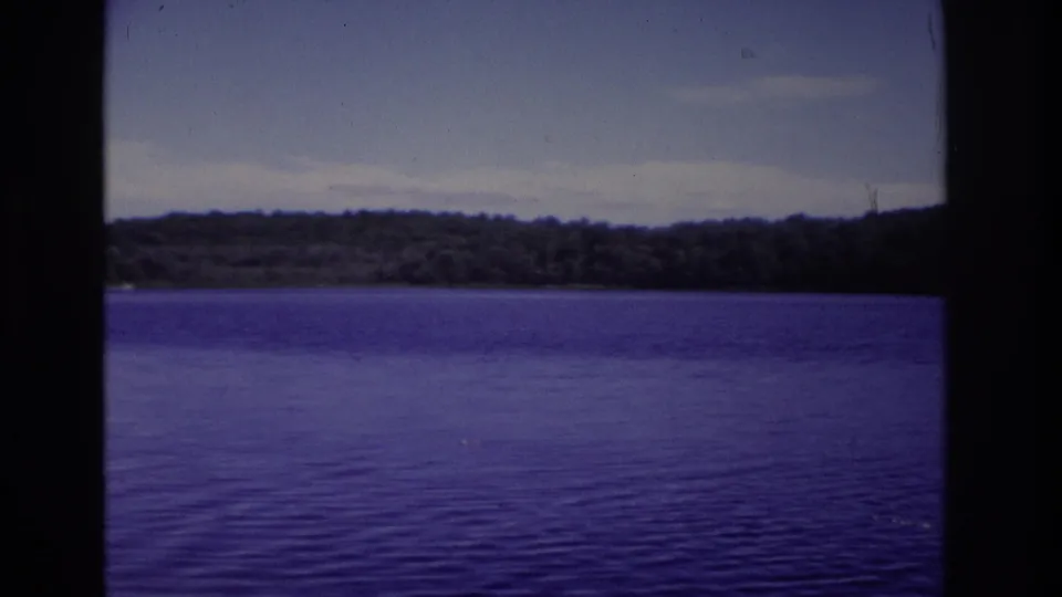 1968 Ocean City, New Jersey 8mm frame holding on open lake water with a distant wooded shore and lightly clouded sky.