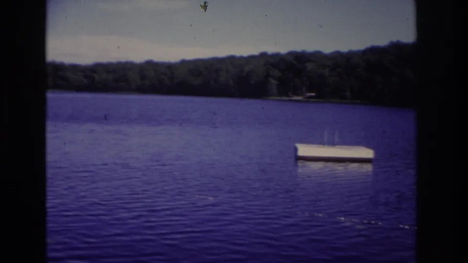 1968 Ocean City lake view with a white floating platform on the water and a wooded shoreline in the distance.