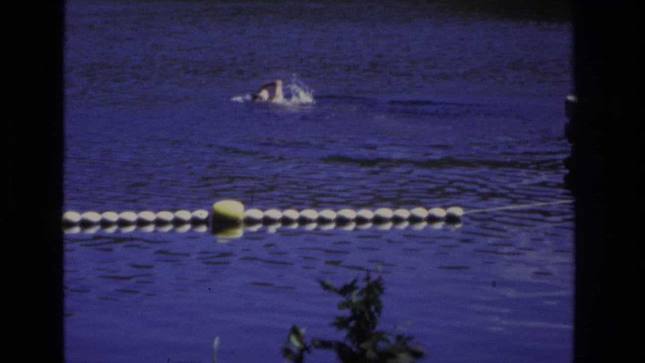 1968 Ocean City home-movie frame with a distant swimmer crossing calm blue water beyond white buoys and a yellow marker.