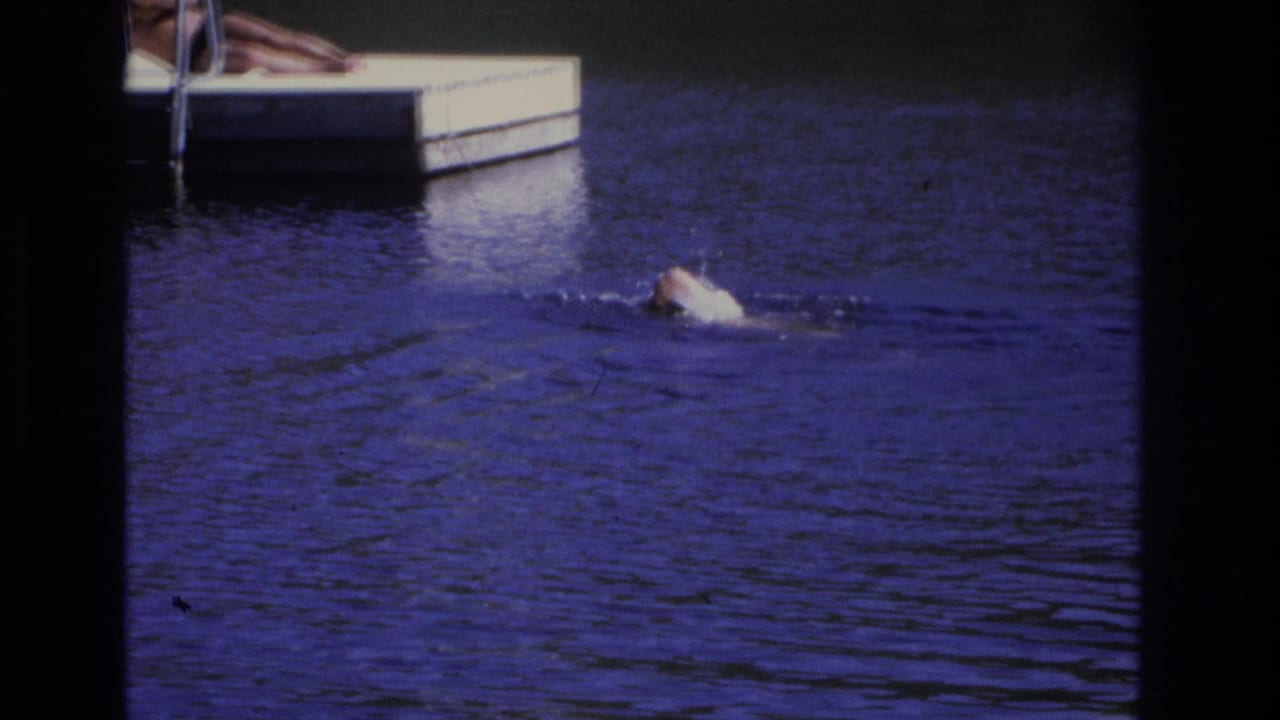 1968 Ocean City home-movie frame showing a monkey swimming toward a dock as a person lies partly visible on the platform.