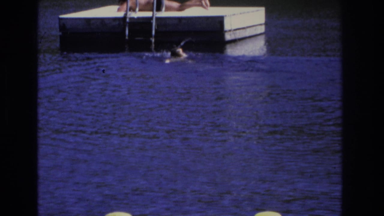 Swimmer reaches the side of a floating dock in blue water.