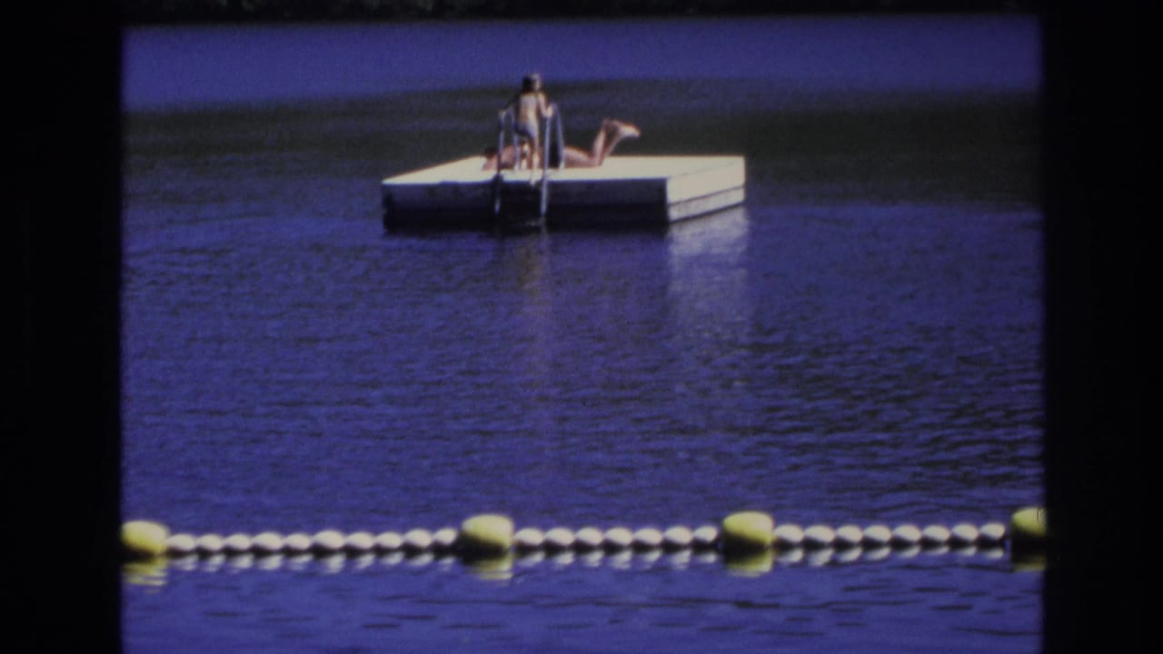 1968 Ocean City, New Jersey home-movie frame showing two people on a white floating dock beyond a yellow and white buoy line.