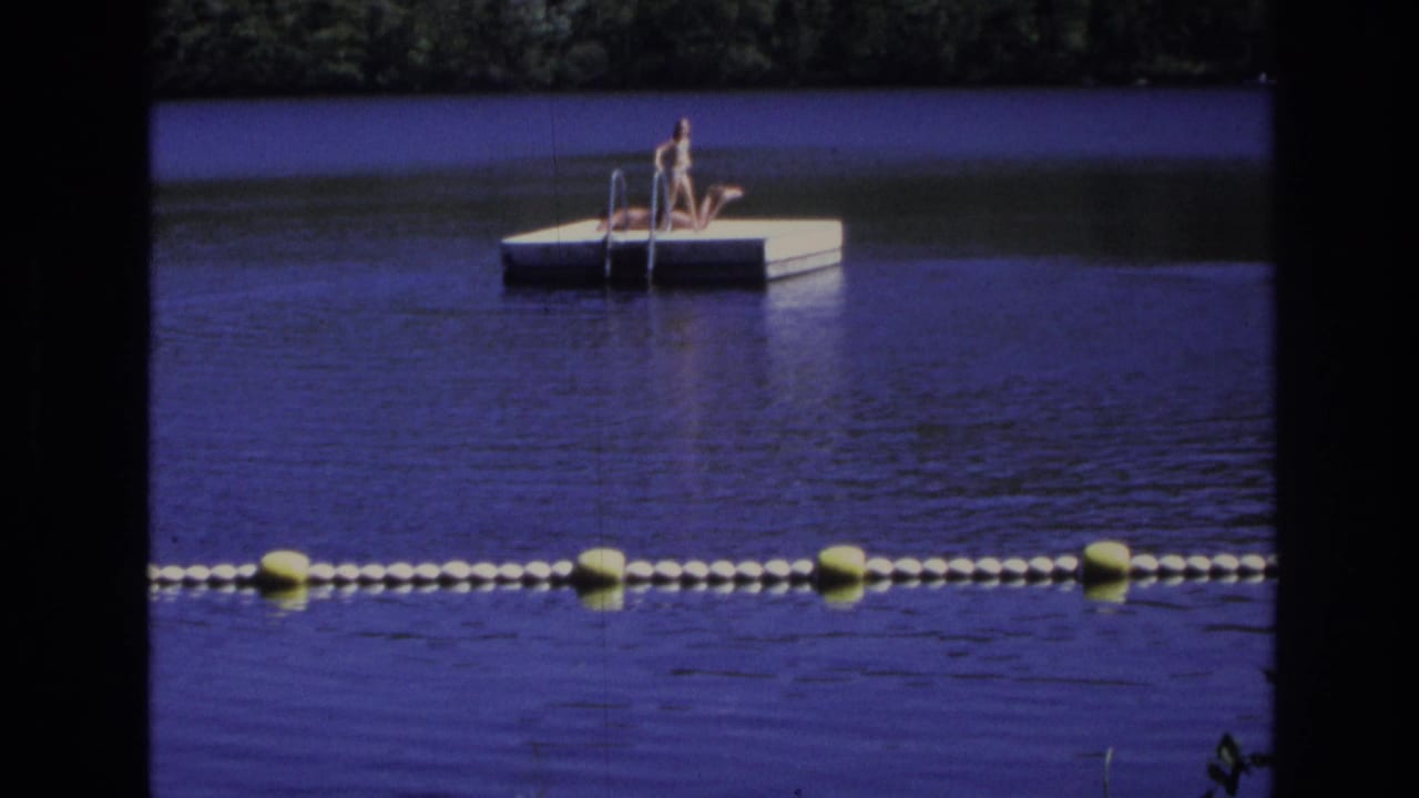 Distant 1968 home-movie view of two people on a floating dock at Ocean City, New Jersey, with buoy markers across the water.