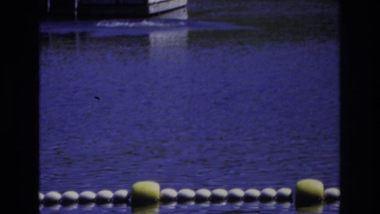 1968 Ocean City home-movie frame showing a buoy-marked swim area seen through dark foreground bars, with rippled blue-purple water.