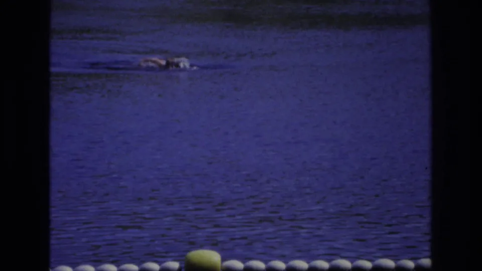 Ocean City 1968 home-movie frame showing a swimmer partly submerged in rippled water below a row of buoys.