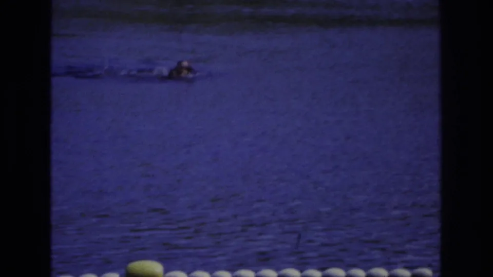 1968 Ocean City frame with a swimmer doing a front-stroke movement in blue-purple water near the buoy-marked area.