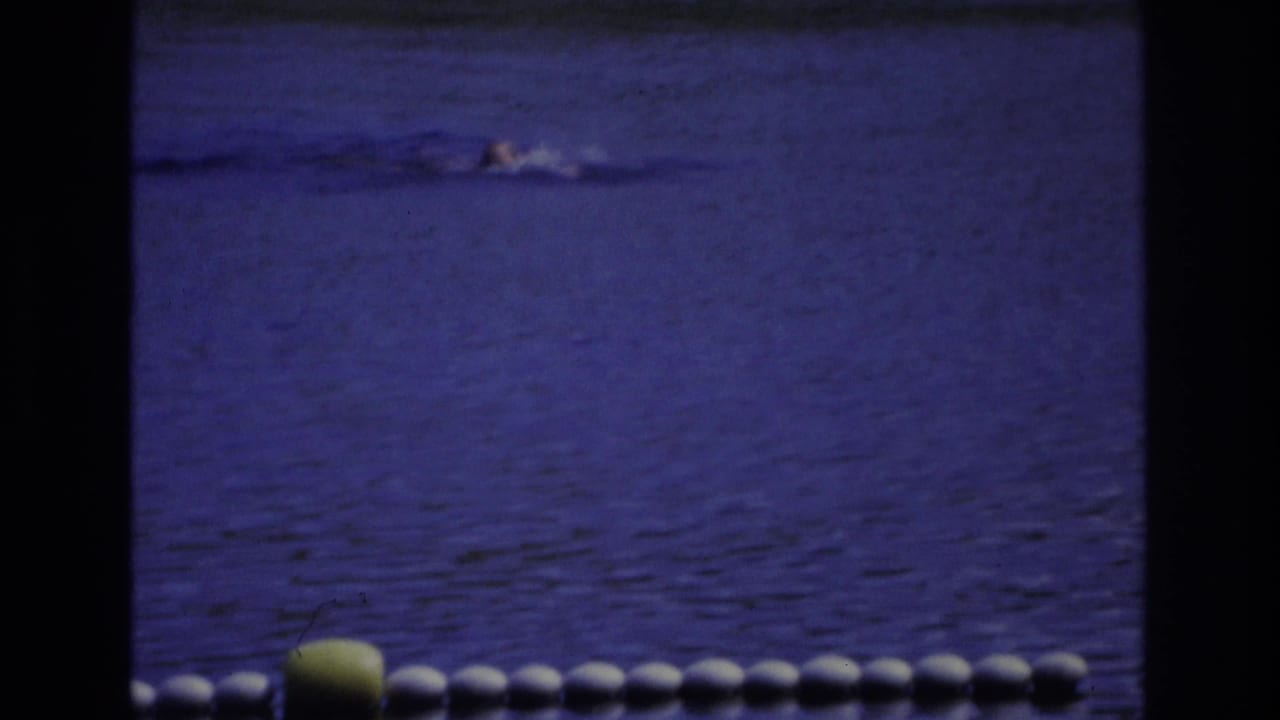 Swimmer crossing blue water behind a white float line and yellow buoy.