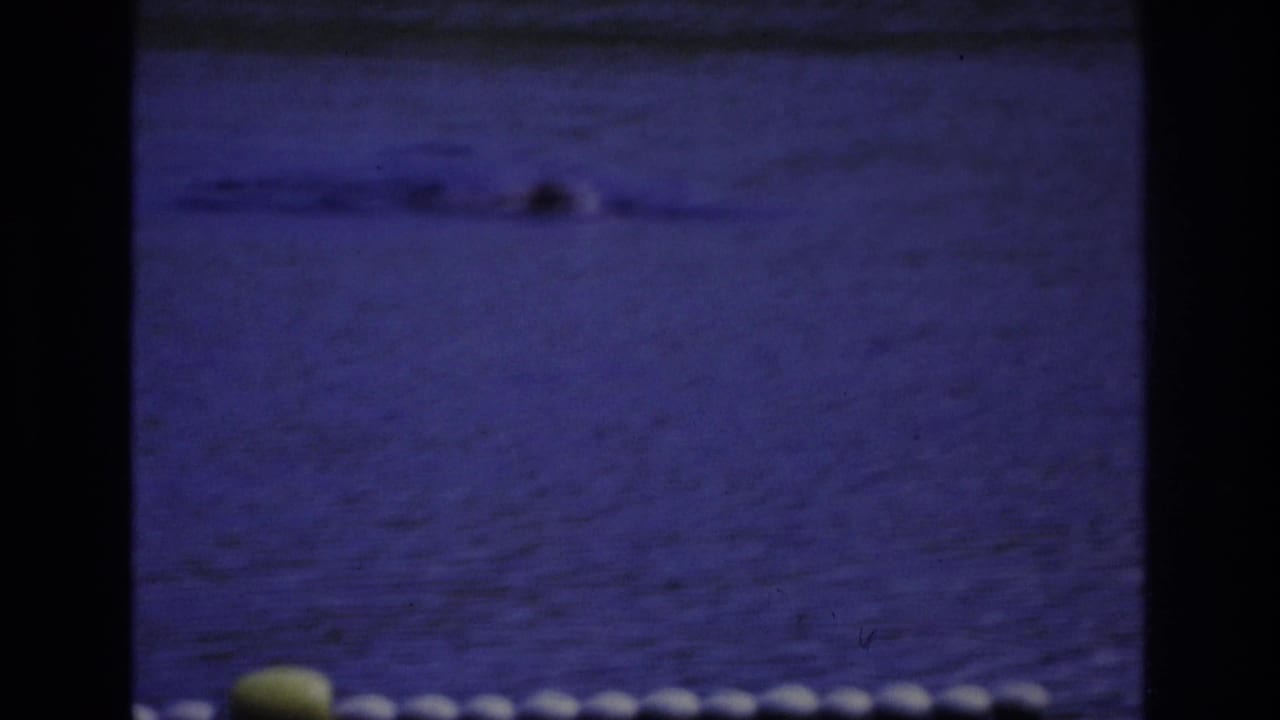 1968 Ocean City frame with a swimmer partly visible in blue water, a float line, and a yellow buoy near the foreground.