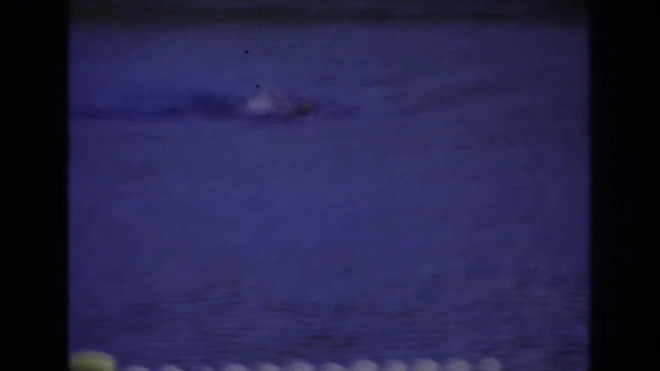 Blue-tinted 8mm frame from Ocean City showing a swimmer low in the frame with ripples spreading across the water.