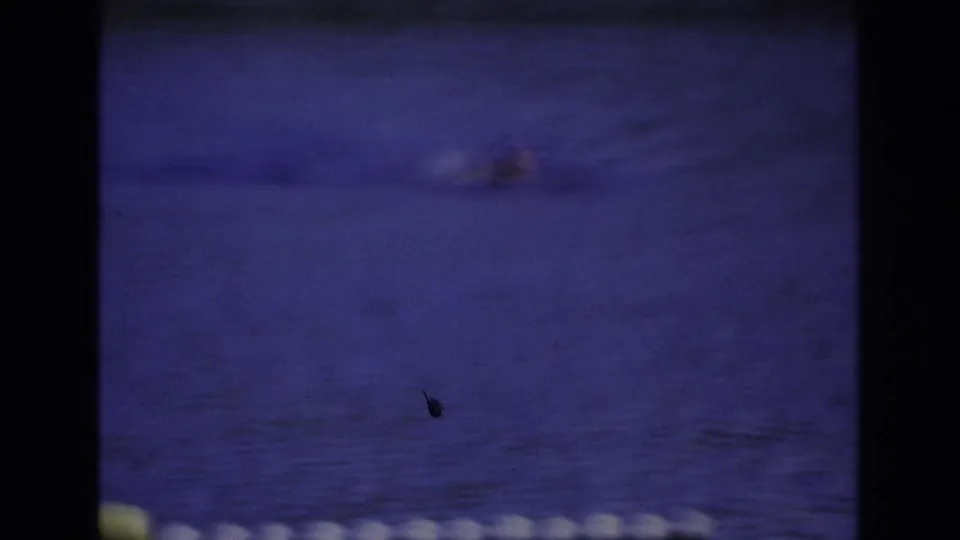 1968 Ocean City home-movie frame showing a swimmer near center-right, blue water, and white floats along the lower edge.
