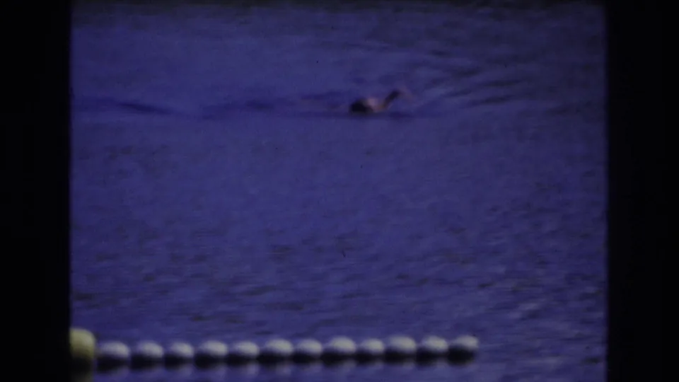 1968 Ocean City home-movie frame showing a distant swimmer beyond a white buoy line in blue-tinted water.