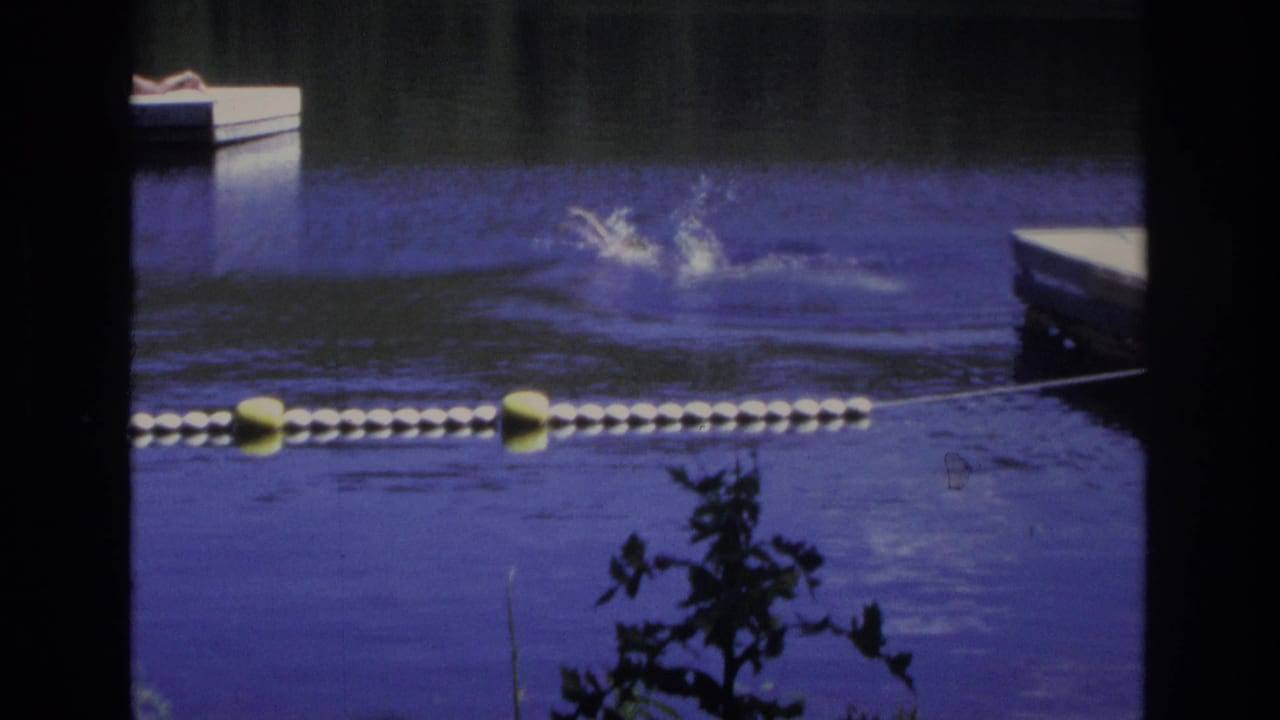 Swimmer splashing in blue water behind a yellow and white buoy line.