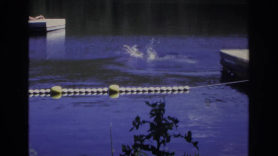 1968 Ocean City home-movie frame showing a swimmer splashing in blue-purple water behind a floating buoy line.