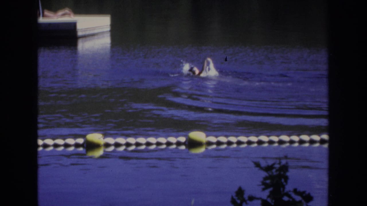 1968 Ocean City footage frame with a swimmer moving across blue-purple water near a dock and foreground buoys.