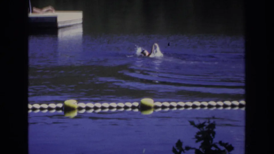 1968 Ocean City footage frame with a swimmer moving across blue-purple water near a dock and foreground buoys.