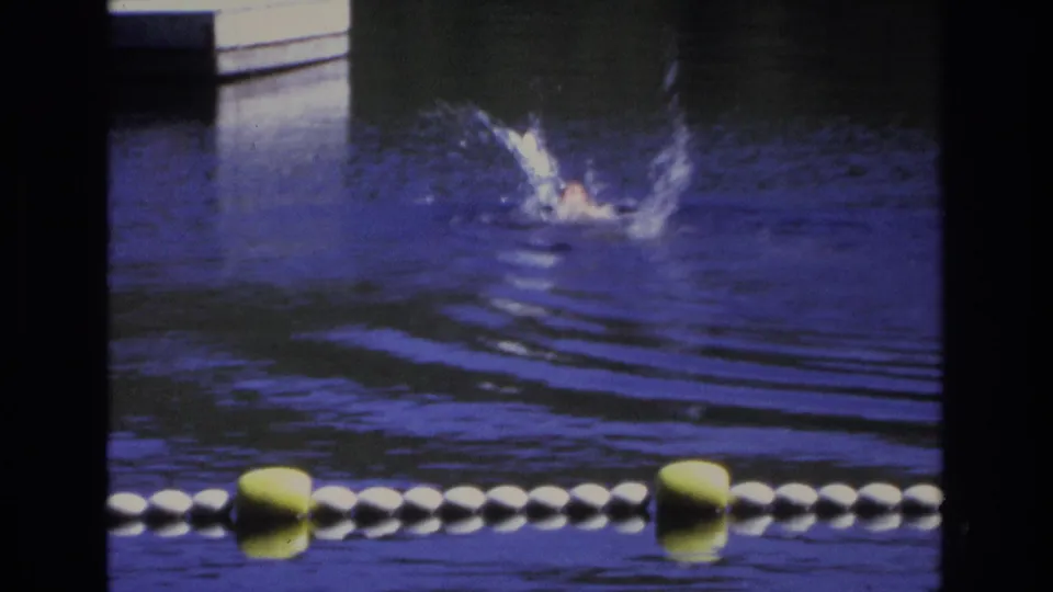 1968 Ocean City home-movie still showing a swimmer splashing through blue-purple water behind yellow and white buoys.