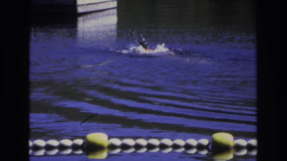 1968 Ocean City frame showing a swimmer crossing blue-purple water, with ripples and a yellow-white buoy line in front.