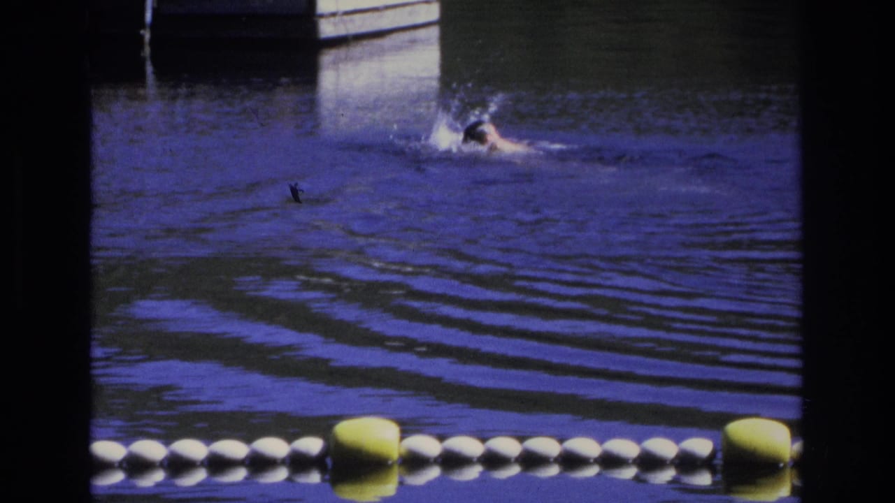 Swimmer splashing through blue water behind a white and yellow buoy line.
