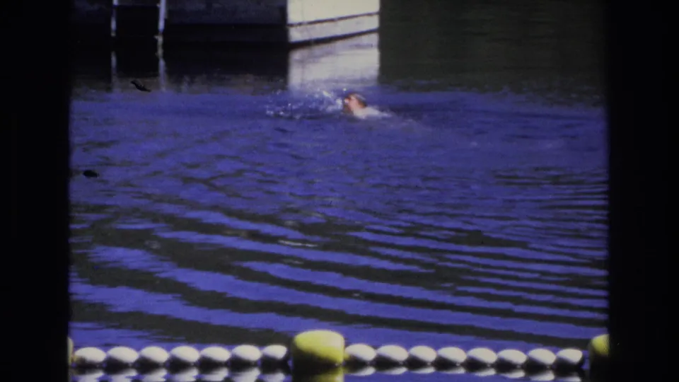 1968 Ocean City home-movie frame with a swimmer partly visible in blue water, buoy line in front, and dock pilings behind.