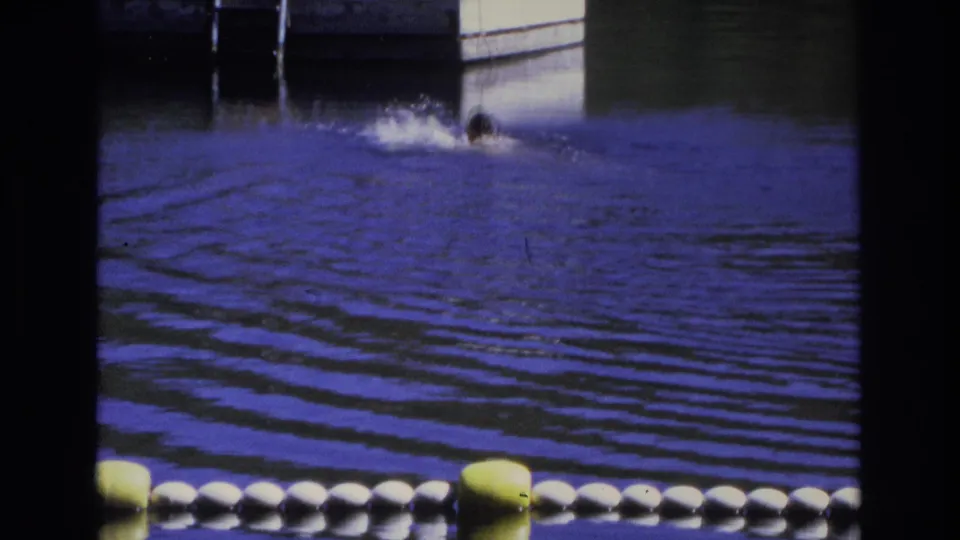1968 Ocean City 8mm frame showing a swimmer surfacing in blue water beyond a foreground line of white and yellow floats.