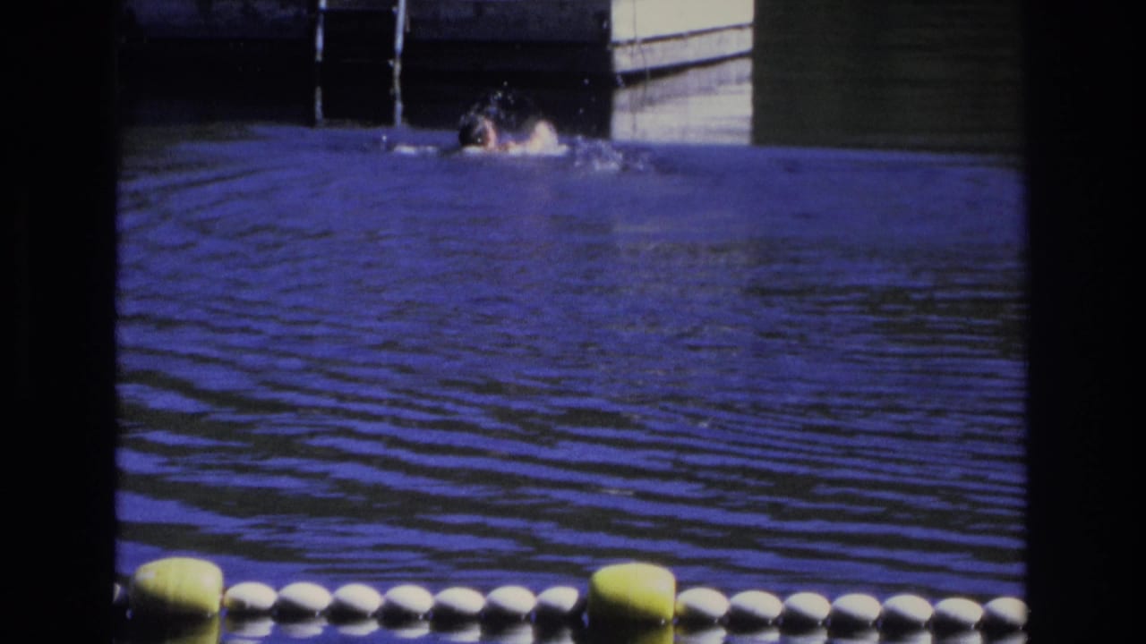 1968 Ocean City home-movie frame showing a swimmer in rippled blue water near a floating dock and metal ladder.