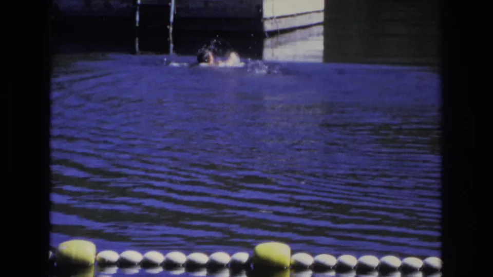 1968 Ocean City home-movie frame showing a swimmer in rippled blue water near a floating dock and metal ladder.
