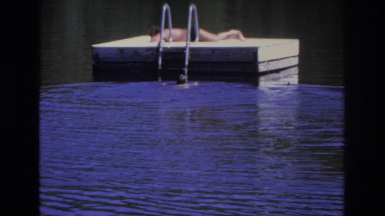 Person lying on a floating dock above rippling blue water with a metal ladder nearby.