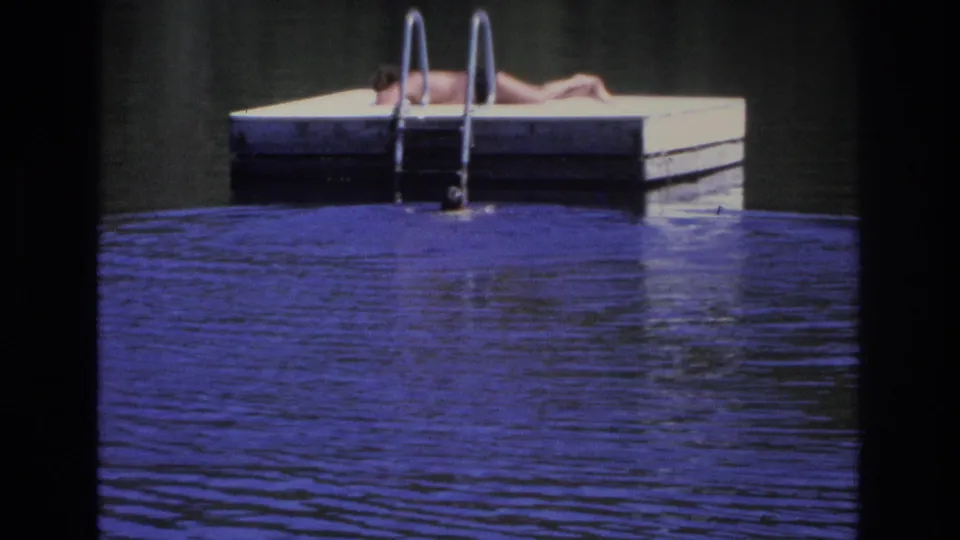 1968 Ocean City home-movie frame showing a person sunbathing on a floating dock beside calm blue water and a metal ladder.